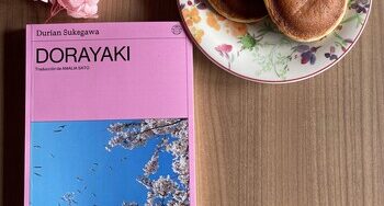 Libro Dorayaki de Durian Sukegawa con portada rosa junto a un plato con dorayakis tradicionales sobre una mesa de madera.