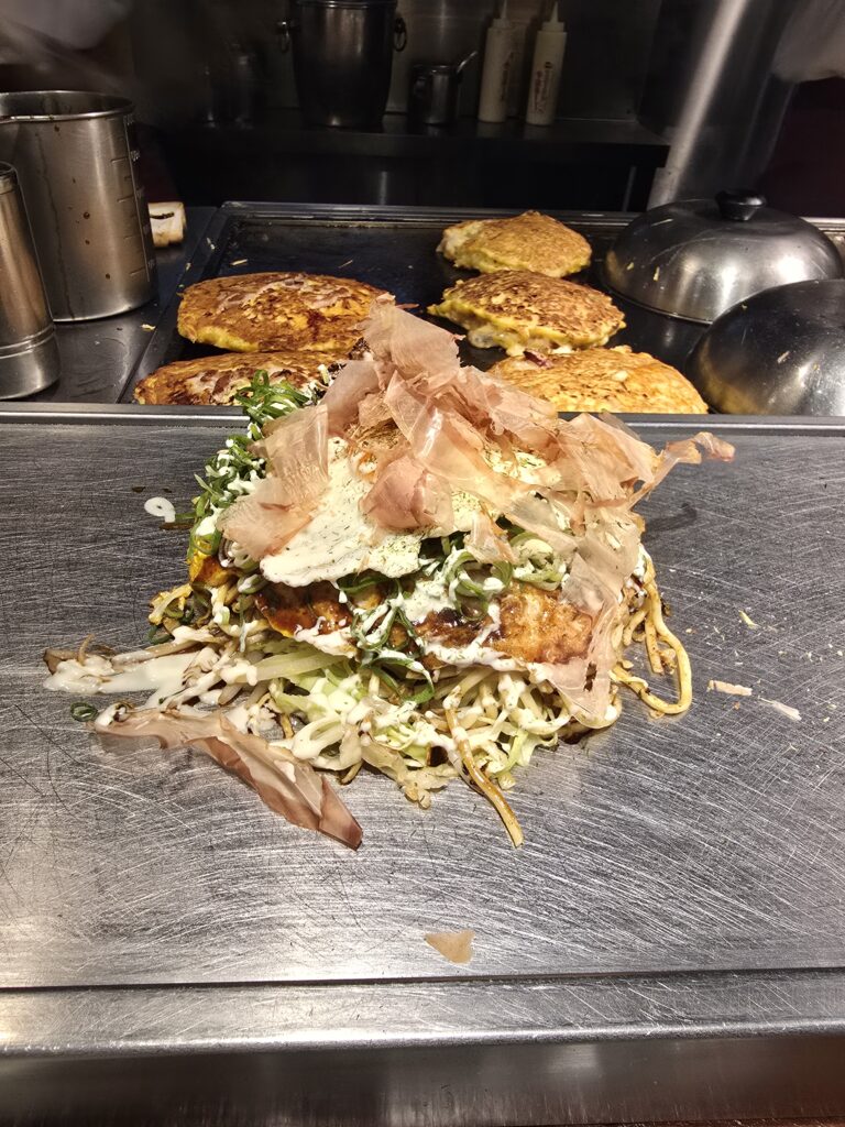 okonomiyaki, una popular tortilla o crepe salado japonés cocinado a la plancha y cubierto con virutas de bonito seco (katsuobushi), salsa y mayonesa