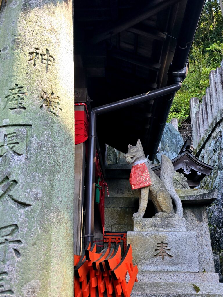 Estatua de zorro de piedra o kitsune adornada con un pañuelo rojo en el santuario Fushimi Inari-taisha de Kioto.