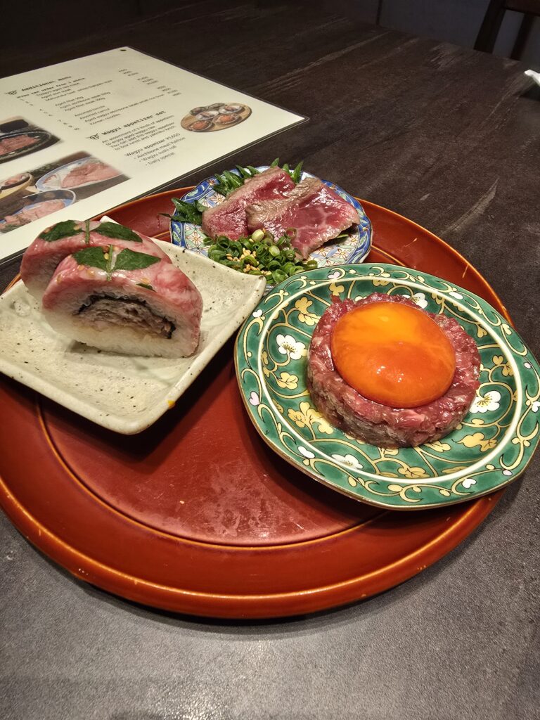 selección de platos de carne cruda de estilo japonés, un tartar de carne con yema de huevo (yukhoe), rollos de sushi o makis de carne y finas lonchas de wagyu