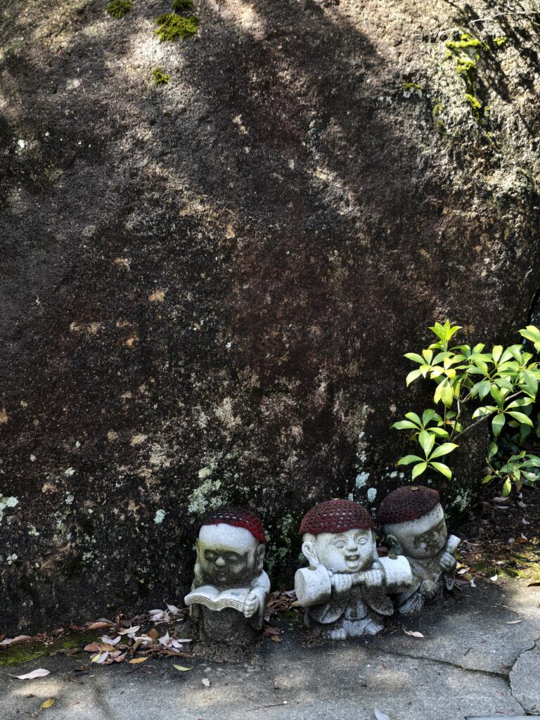 Pequeñas estatuas de piedra de Jizō con gorritos rojos tejidos, ubicadas en caminos de templos o montañas en Japón, como en la isla de Miyajima