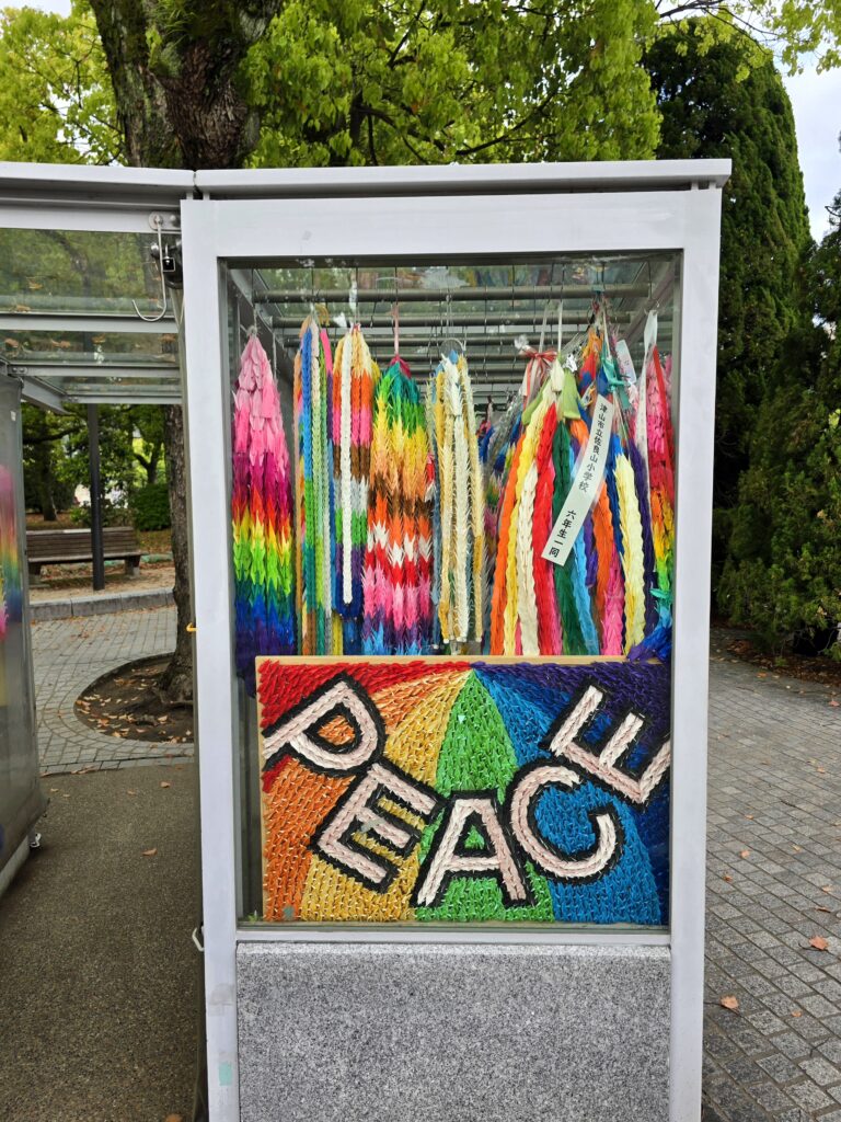 urna de cristal en el Parque de la Paz de Hiroshima (Japón), llena de coloridas guirnaldas de grullas de papel (senbazuru) y un letrero con la palabra "PEACE"