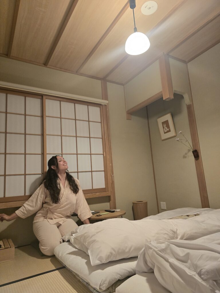Viajera disfrutando de la comodidad de un ryokan tradicional en Japón, sentada en una habitación con paredes de tatami y ventanas shoji de papel.