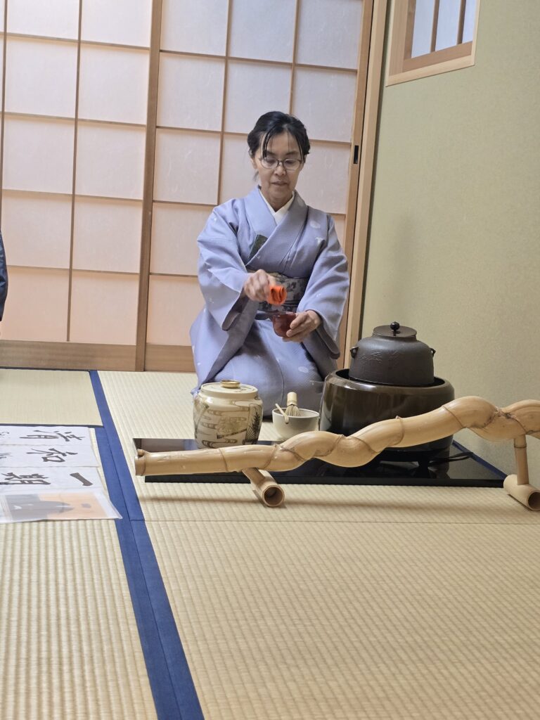 persona oficiando una ceremonia del té tradicional japonesa en una estancia decorada con esteras de tatami.