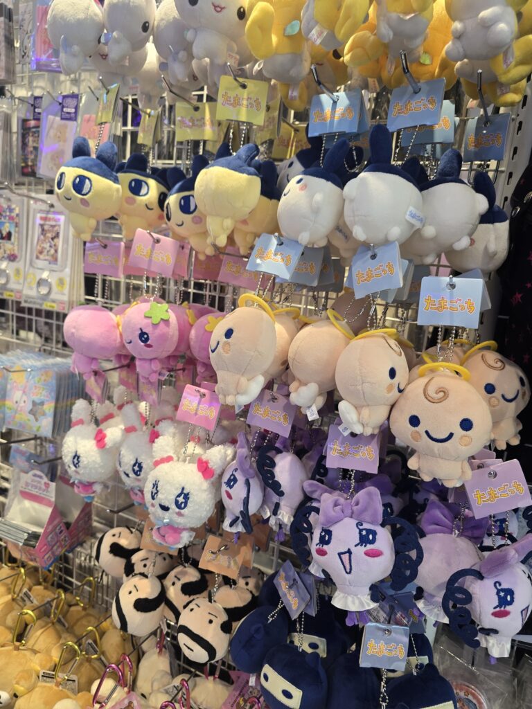 estante con una variedad de llaveros de peluche y juguetes de los personajes de Tamagotchi, incluyendo figuras como Mametchi y Oyajitchi.