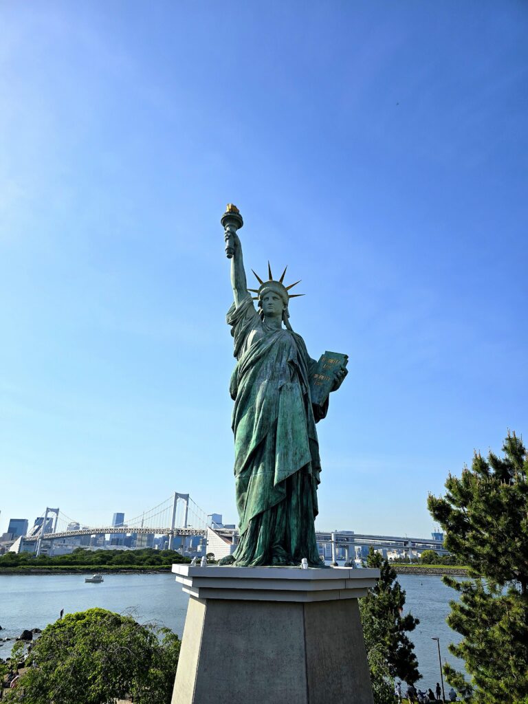 réplica de la Estatua de la Libertad ubicada en la isla artificial de Odaiba, en la bahía de Tokio, Japón, con el Puente Arcoíris al fondo