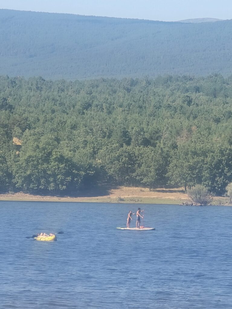 Deportes acuáticos en Playa Pita, Soria, con bañistas en tablas de paddle surf rodeados de pinares.