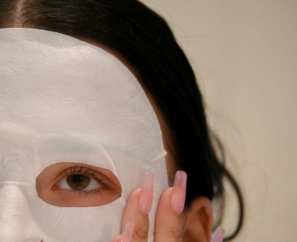 persona aplicándose una mascarilla facial de tejido de color blanco.