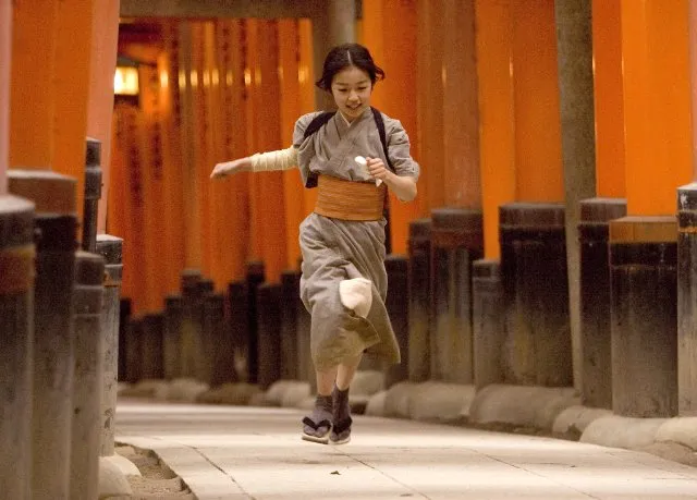 Niña corriendo por los túneles de puertas torii naranjas en el santuario Fushimi Inari-taisha de Kioto, Japón, recreando una escena de la película Memorias de una geisha.
